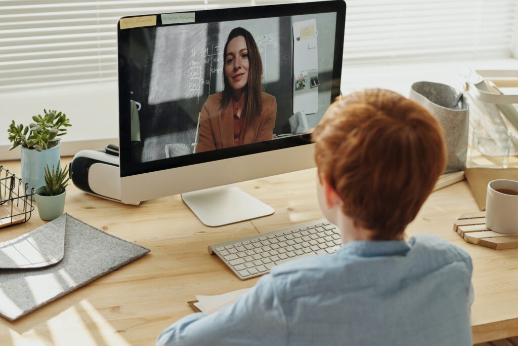 A student learns from a virtual teacher while sitting at a desk in a classroom setting.